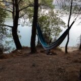Hamac prins între doi copaci pe malul unui lac liniștit, într-o după-amiază de vară