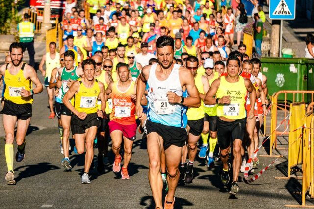 Alergători amatori care participă la o cursă de semimaraton pe o stradă din oraș, într-o dimineață însorită